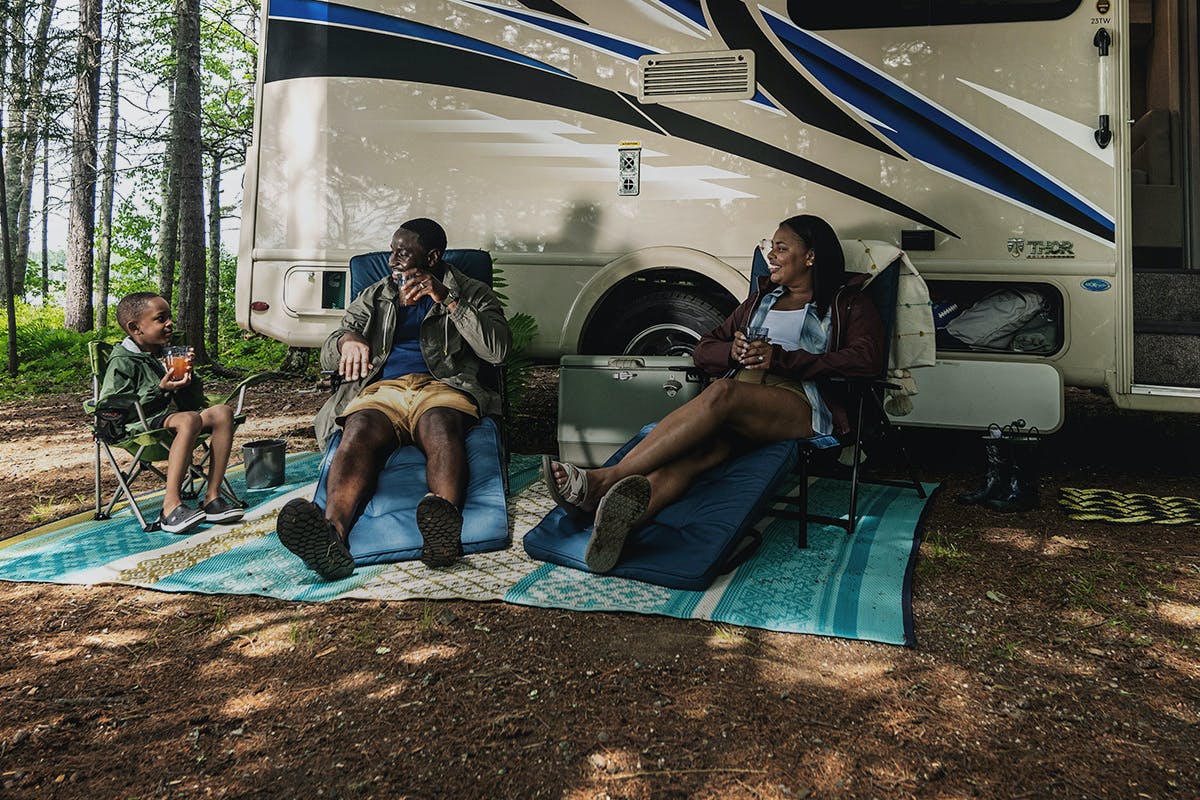 A family smiling at each other while sitting in the shade outside of their RV